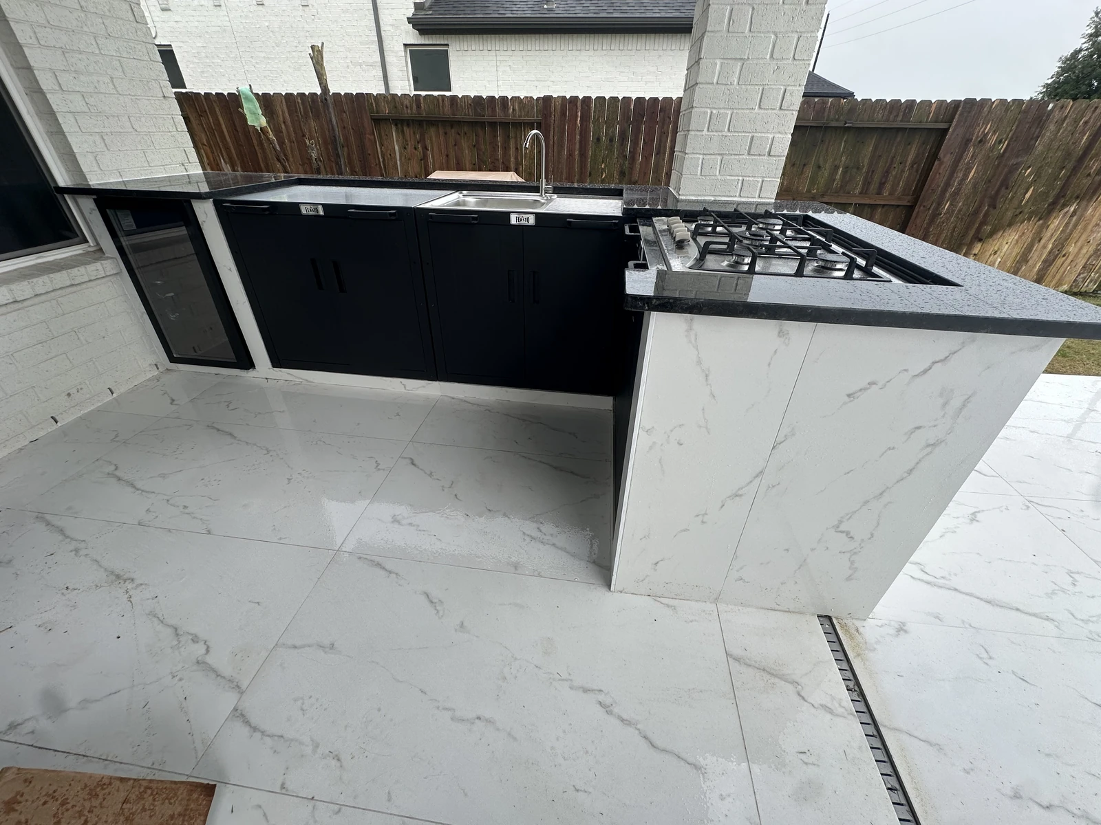 Finished outdoor kitchen with quartz countertops, black cabinetry and a built in gas cooktop in Houston TX