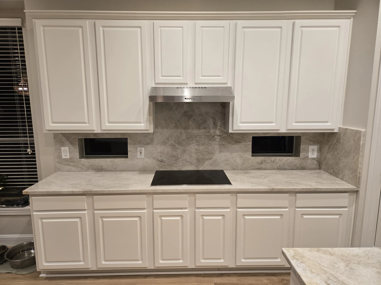 White cabinet kitchen with a marble look quartz backsplash and cooktop in a Houston remodel