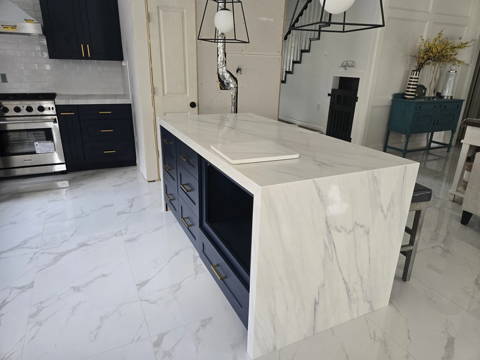Modern kitchen with a navy island and white waterfall quartz counter on marble look tile in Houston