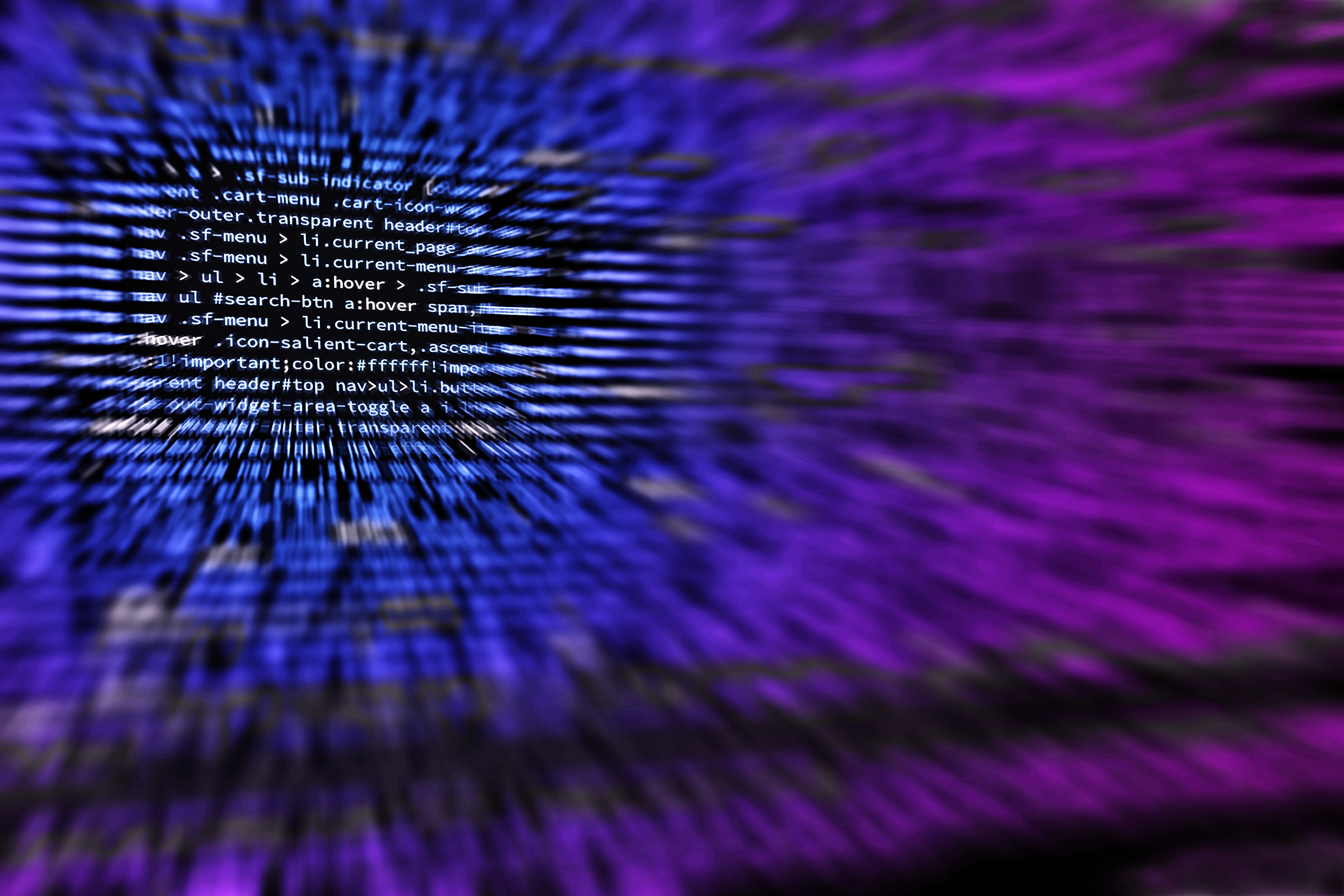 Close-up view of computer screen showing blurred lines of blue and white code with a radial zoom blur effect against a dark purple background.