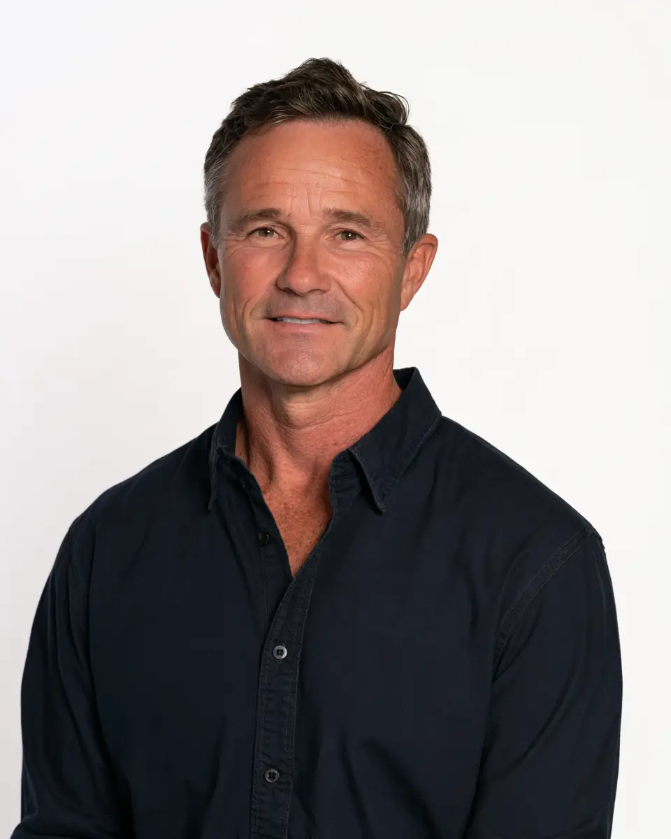 A headshot of a middle-aged man with short brown hair, wearing a dark button-down shirt against a neutral white background.