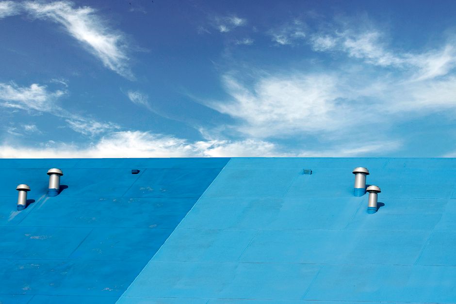 A vibrant blue roof with chimneys under a clear blue sky with scattered clouds, captured outdoors.
