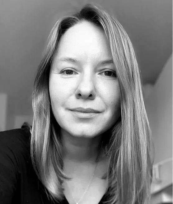 Black and white close-up portrait of a woman with straight shoulder-length hair, wearing a dark top, looking directly at the camera with a neutral expression.