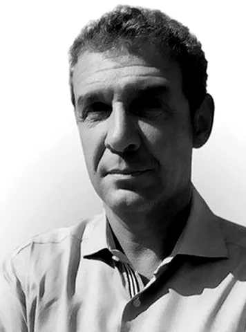 Black and white portrait of a middle-aged man with short curly hair wearing a collared shirt, looking slightly to the side with a neutral expression.