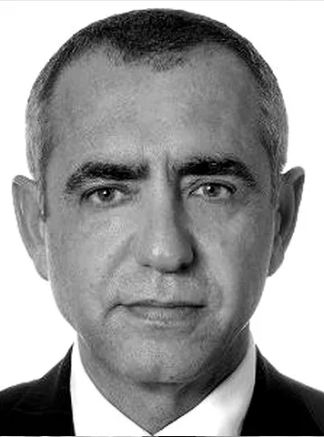 Black and white portrait of a middle-aged man with short hair, wearing a suit and white shirt, looking directly at the camera with a neutral expression.