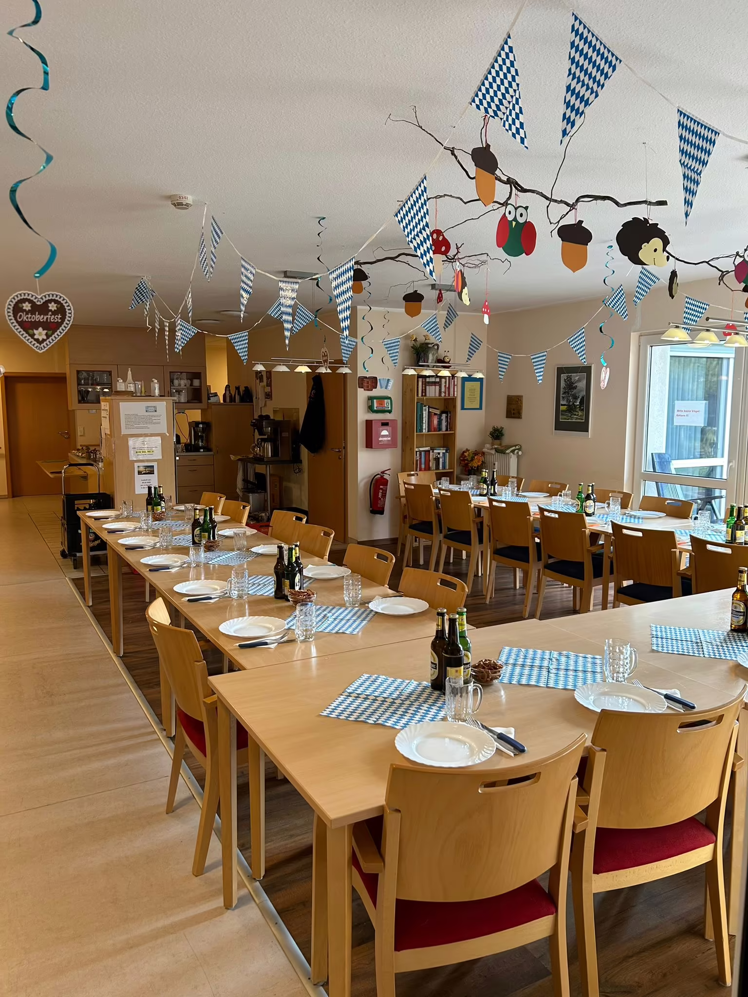 Festlich gedeckte lange Tafel mit blau-wei&szlig;er Oktoberfest-Dekoration auf der Gemeinschaftsfl&auml;che des Seniorenzentrums