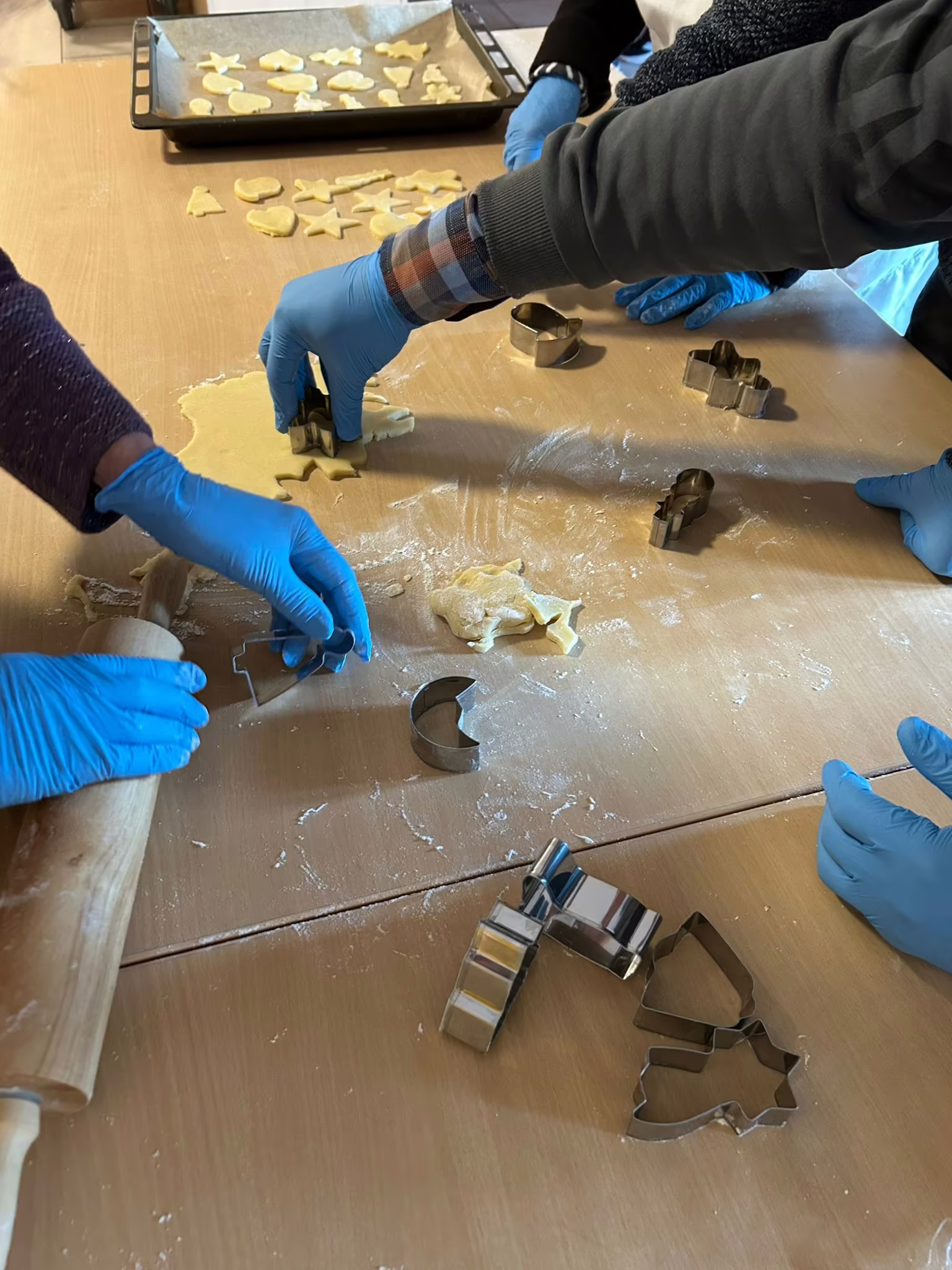 Gemeinsames Pl&auml;tzchenbacken im Seniorenzentrum, mehrere H&auml;nde stechen Weihnachtspl&auml;tzchen aus