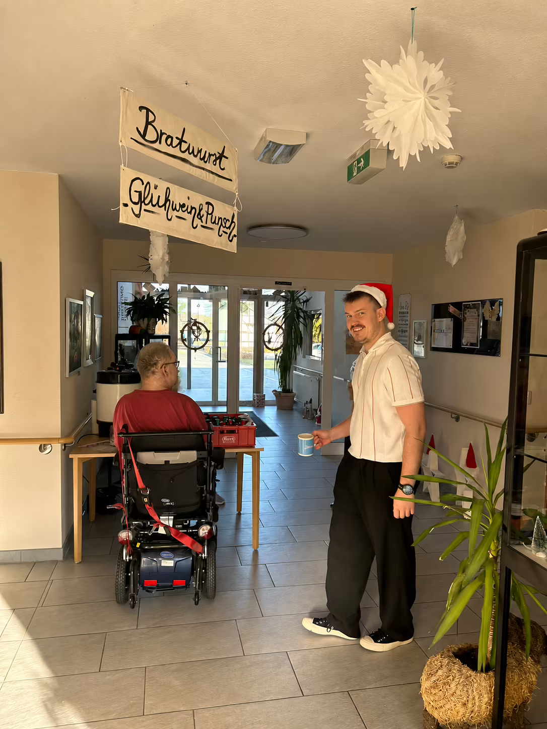 Mitarbeiter des Seniorenzentrums reicht beim Adventsnachmittag einen Becher Punsch unter dem Schild Bratwurst, Gl&uuml;hwein und Punsch