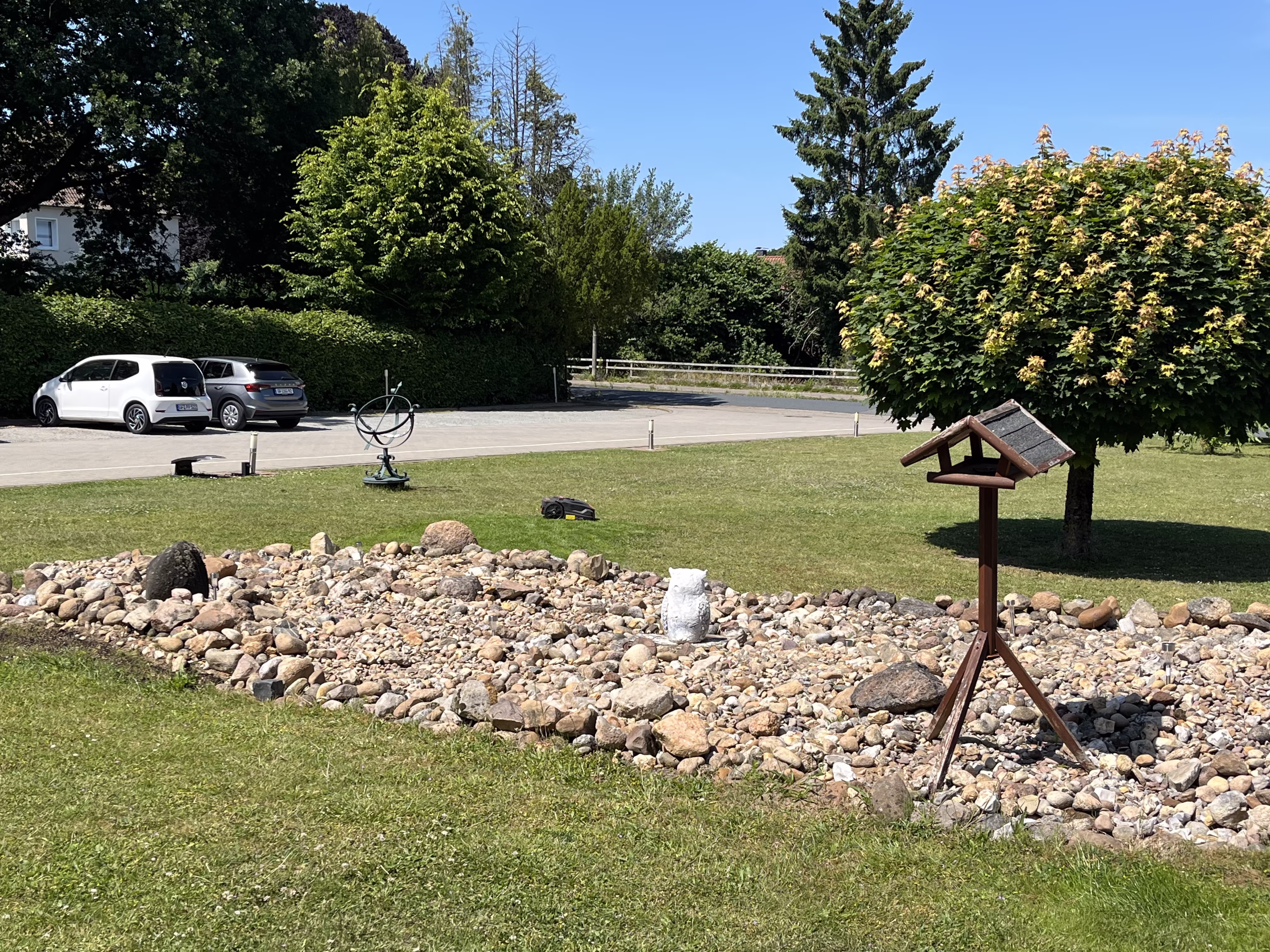Steingarten mit Vogelhaus und Sonnenuhr vor dem Seniorenzentrum, dahinter die Besucherparkpl&auml;tze