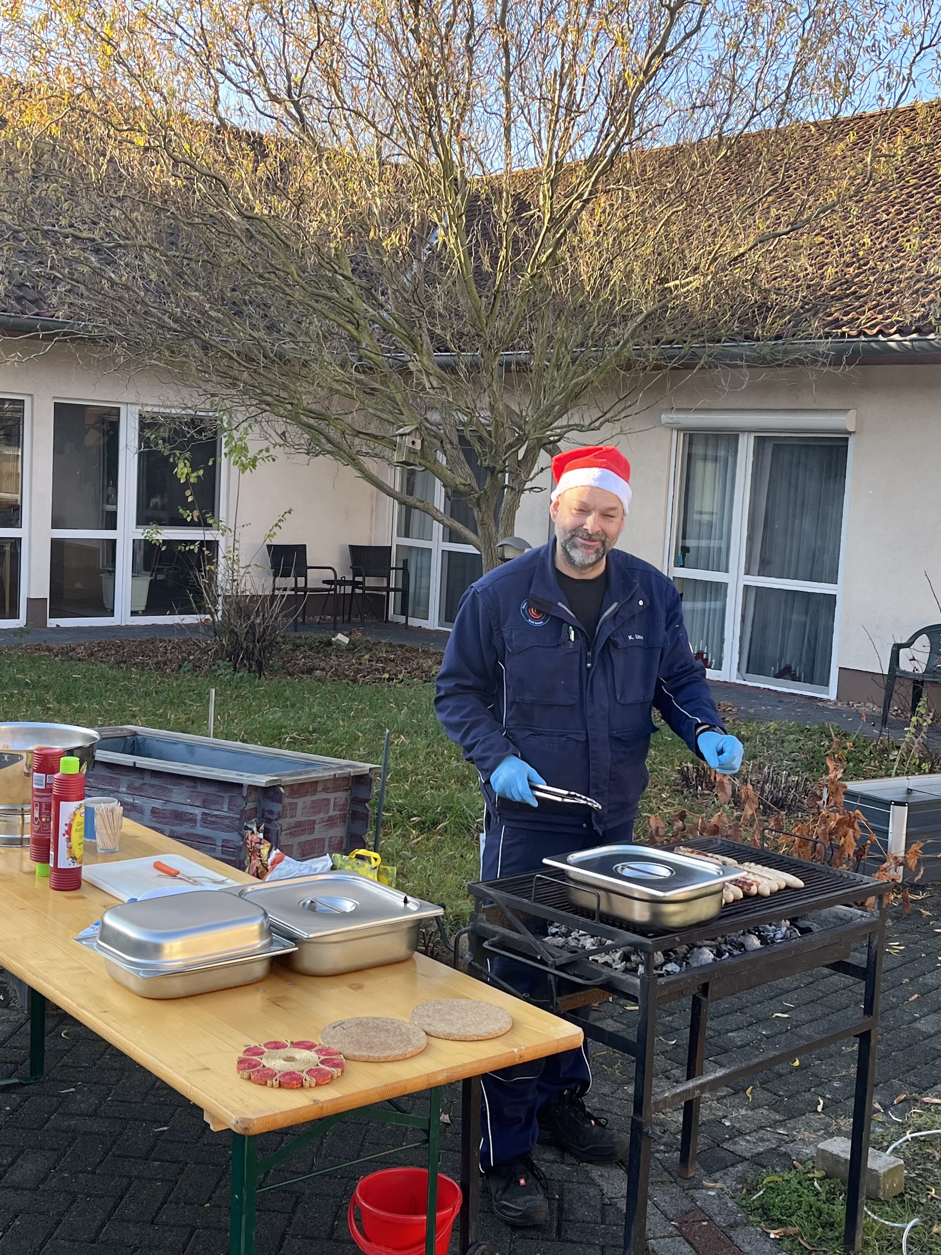 Mitarbeiter des Seniorenzentrums grillt beim Adventsfest Bratw&uuml;rste im Innenhof
