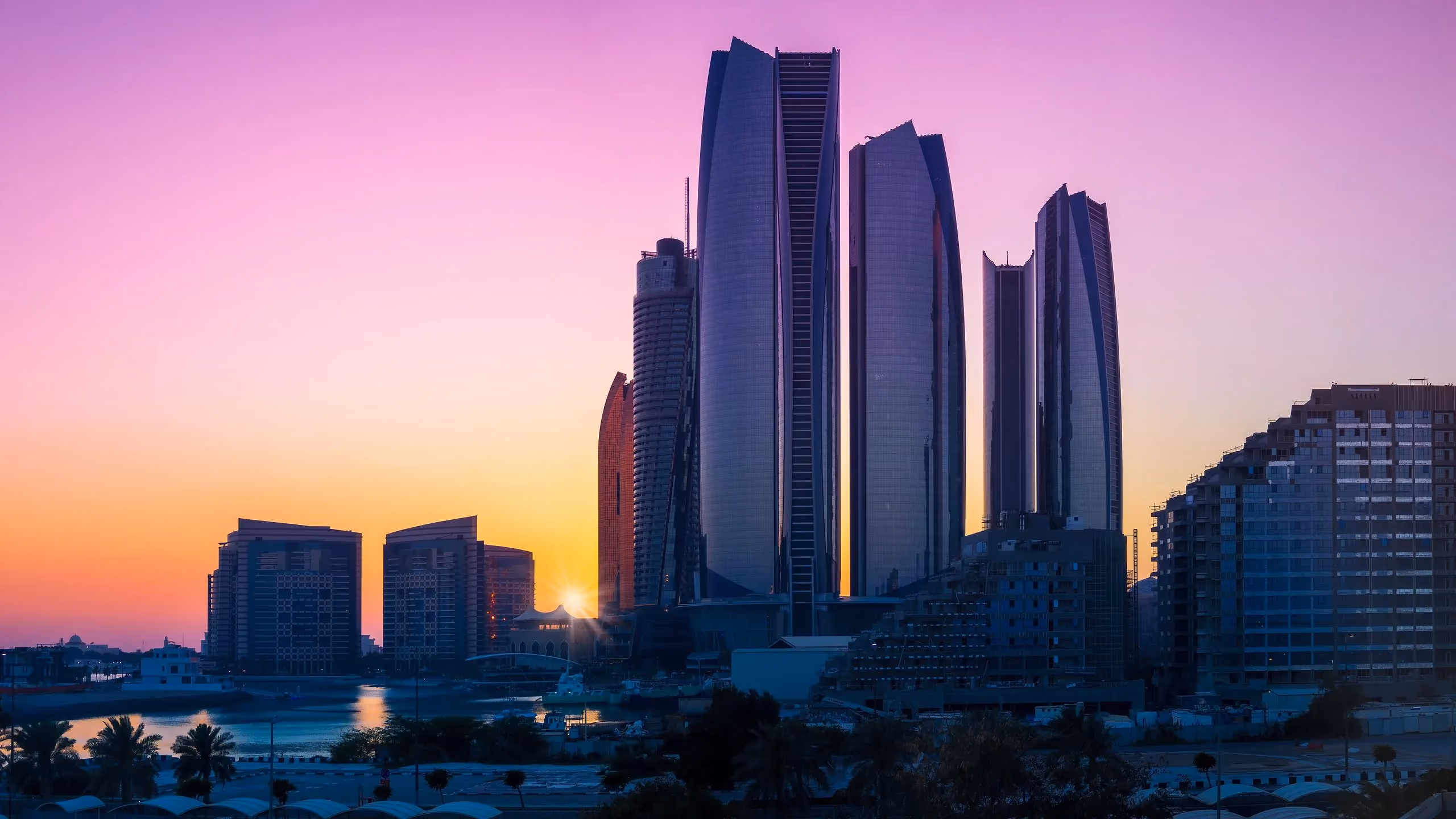City skyline of curved residential towers at sunset, reflected in the water below