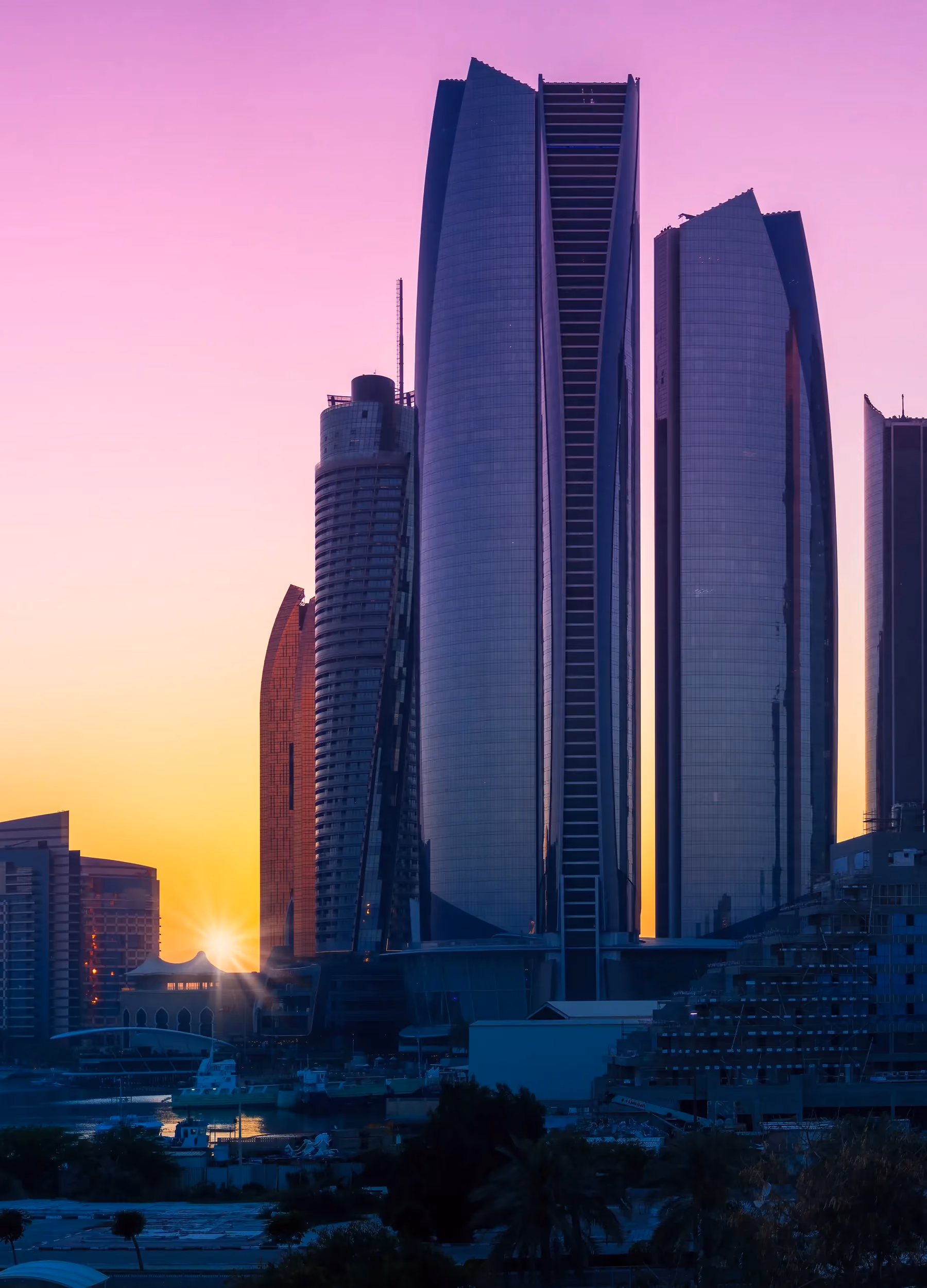 City skyline of curved residential towers at sunset, reflected in the water below
