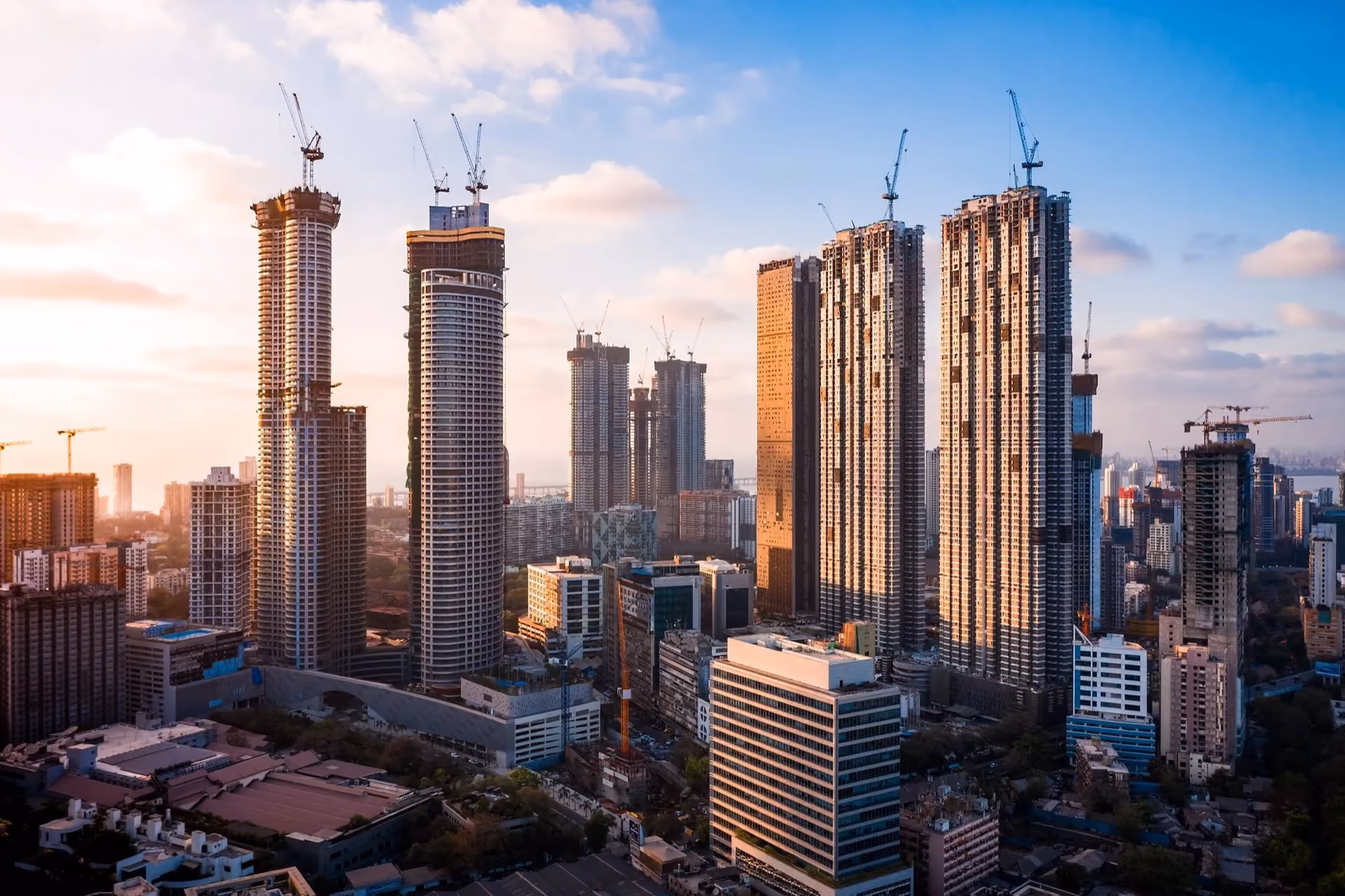 Tall residential towers under construction with cranes at sunset