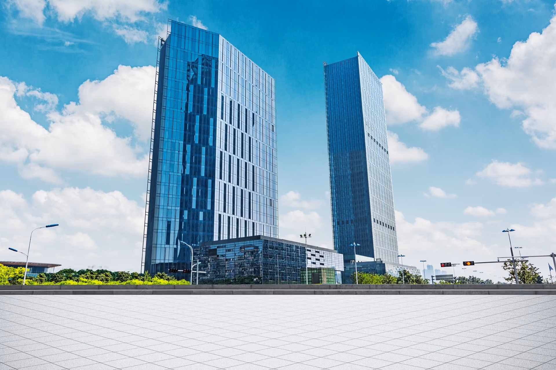 Two slim blue glass towers beyond a pale paved plaza