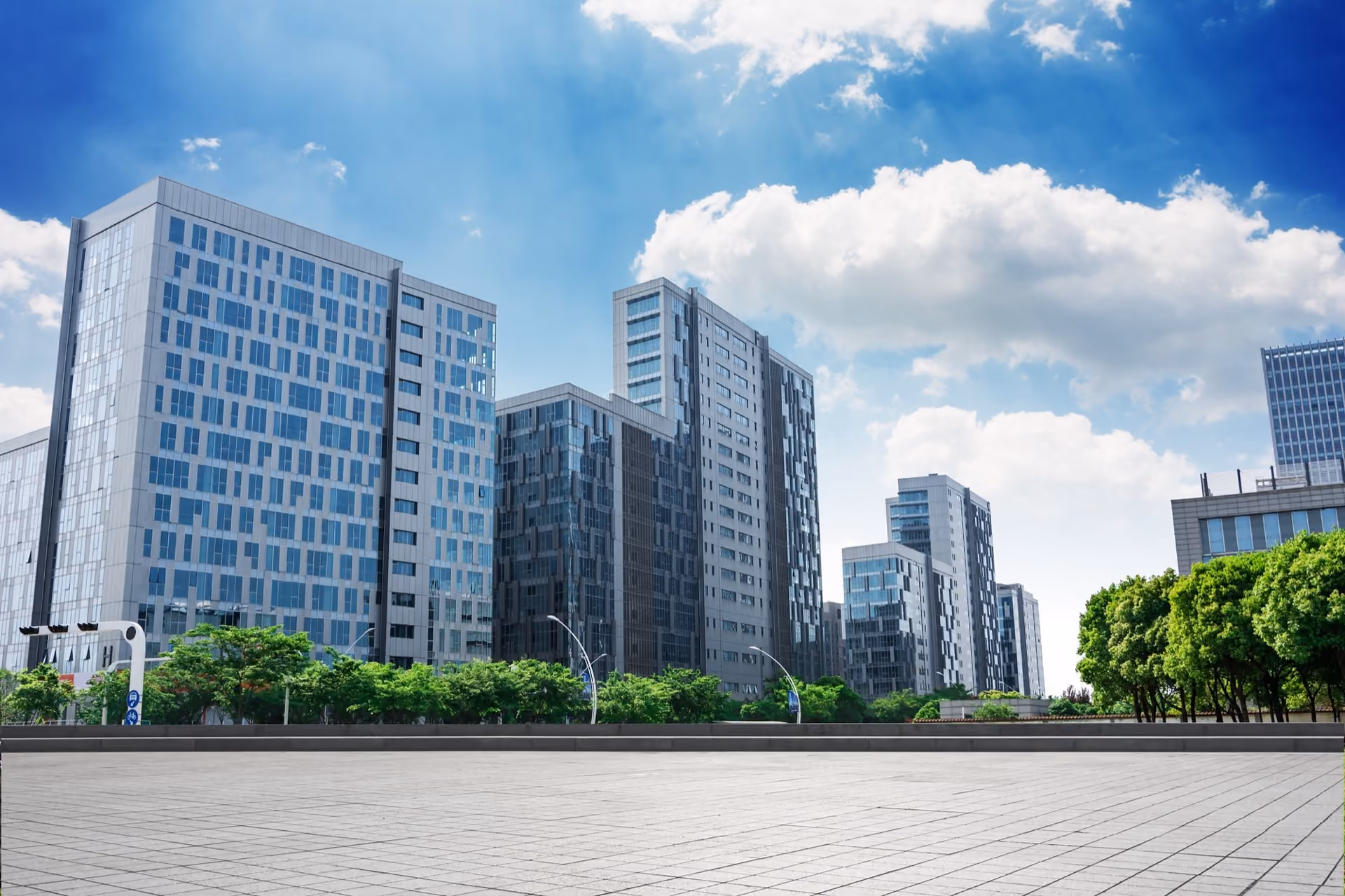Glass office blocks beyond a paved plaza under a bright sky