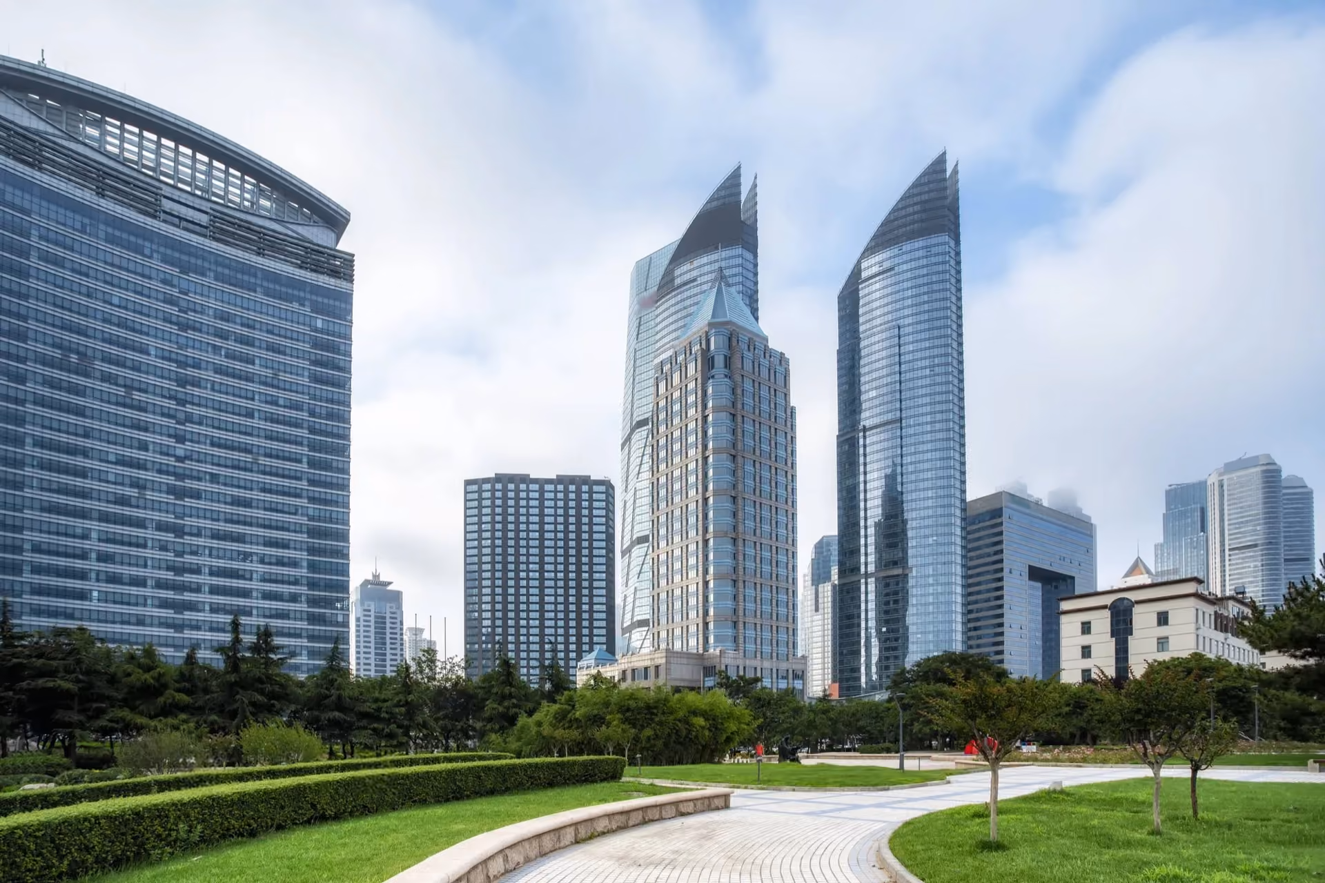 Curved glass towers above a landscaped park with a winding path