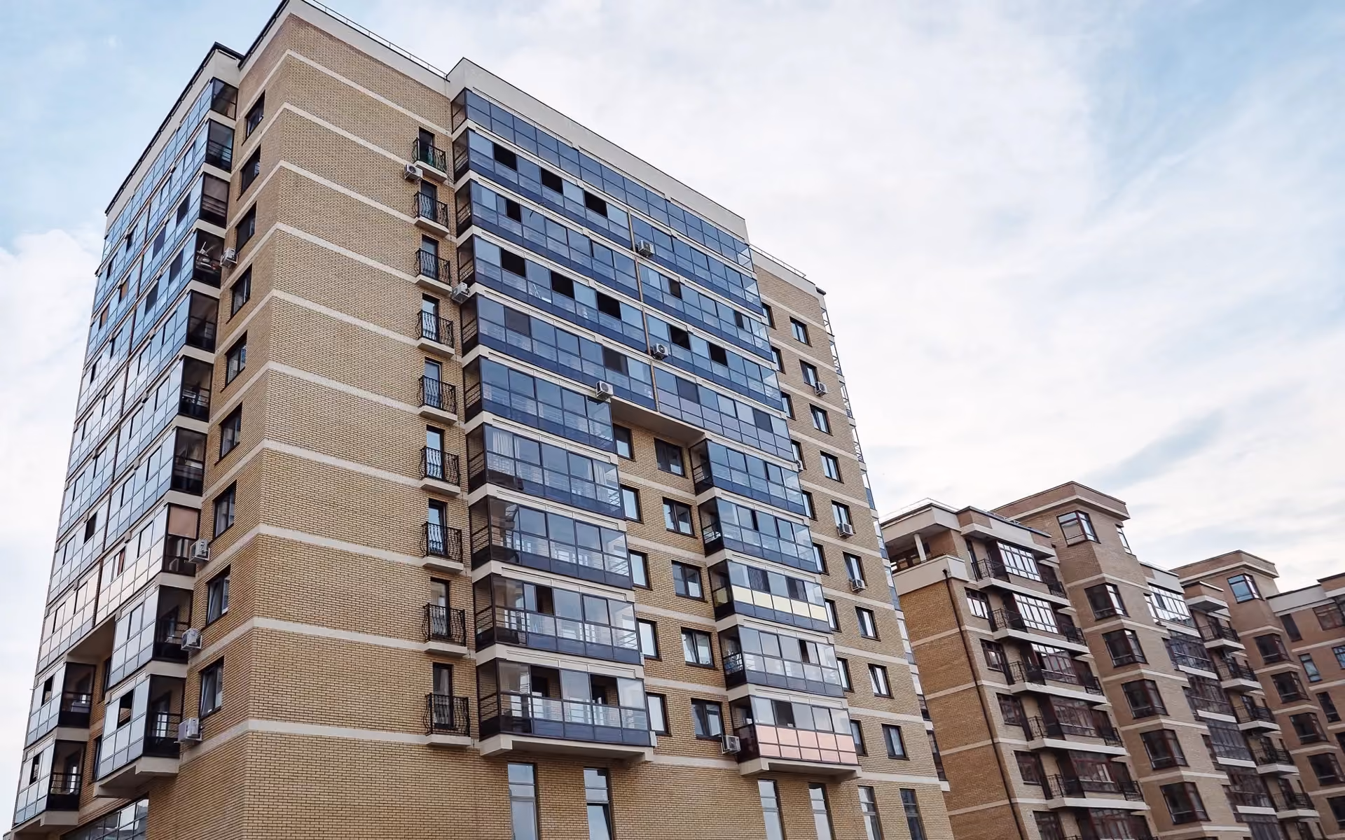Brick and glass apartment towers with balconies under a cloudy sky