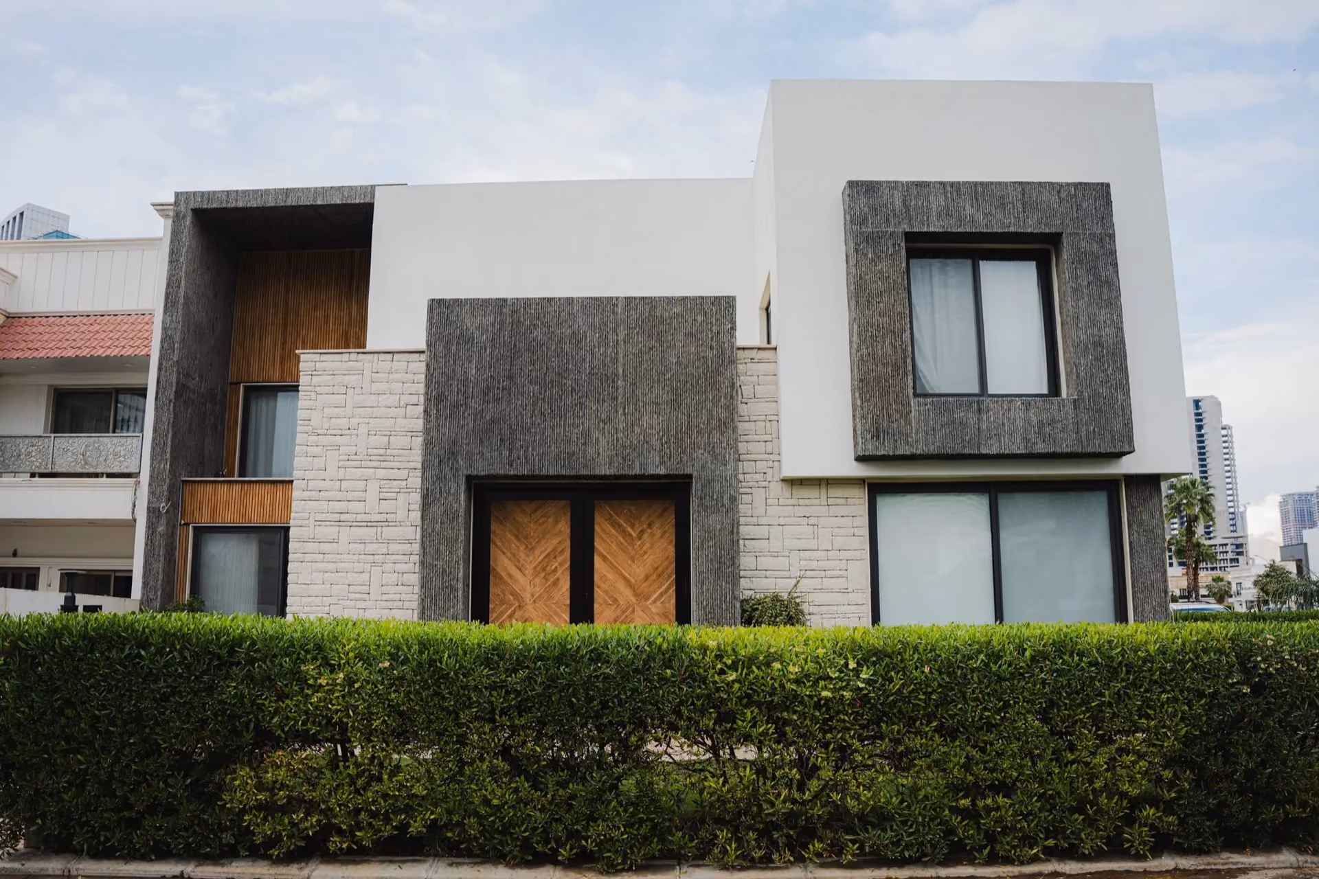 Modern detached house with stone and render facade behind a clipped hedge