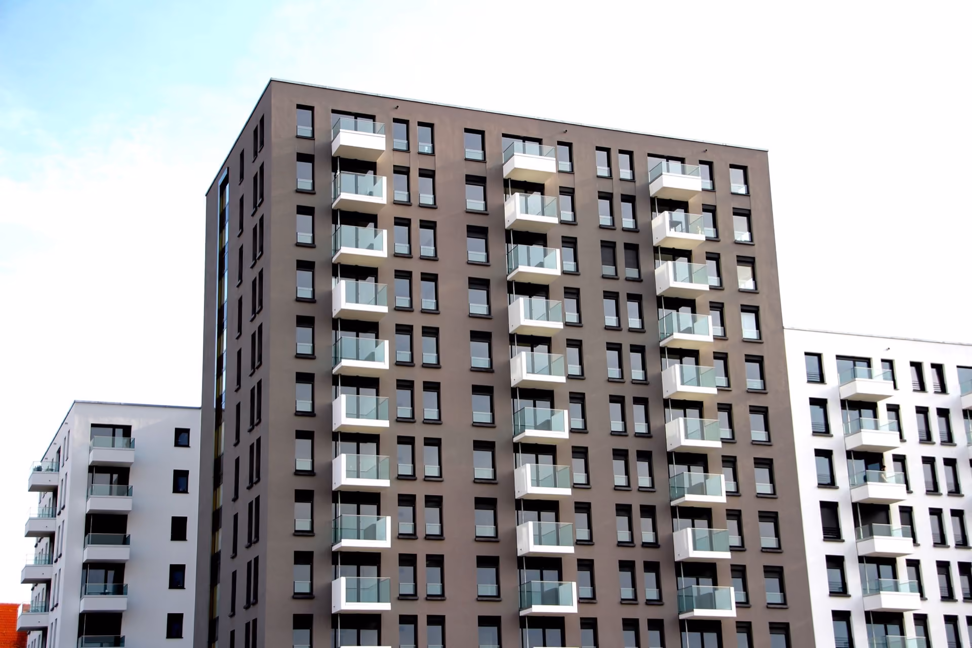 Dark brick apartment block with rows of balconies against a pale sky