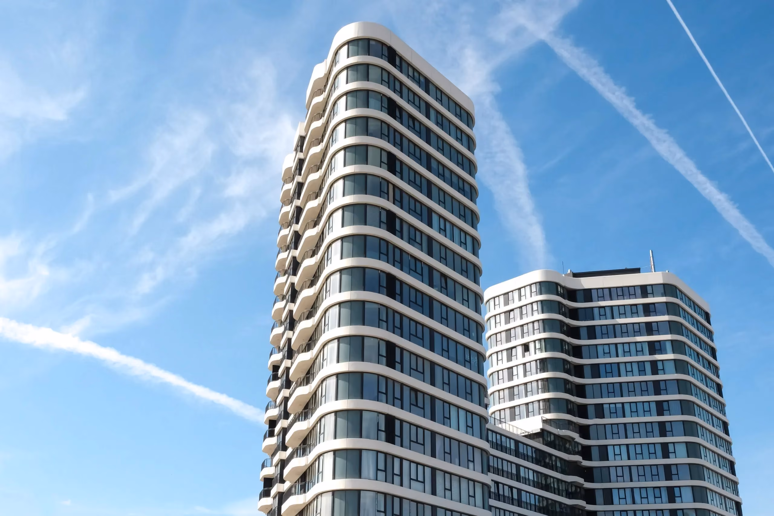 Two white residential towers with curved balconies against a blue sky