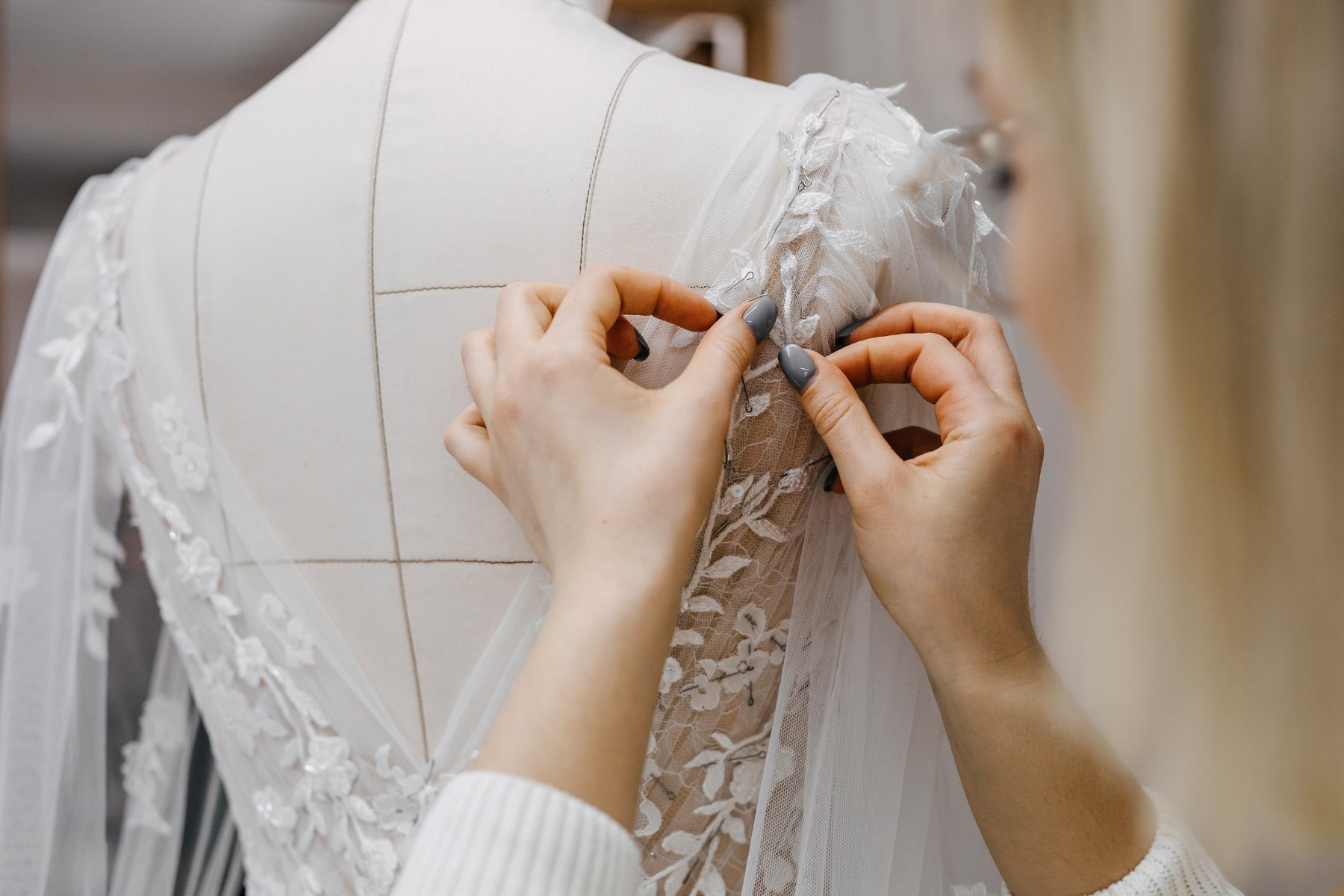 Hands pinning delicate bridal lace onto a marked dress form during the gown-making process.