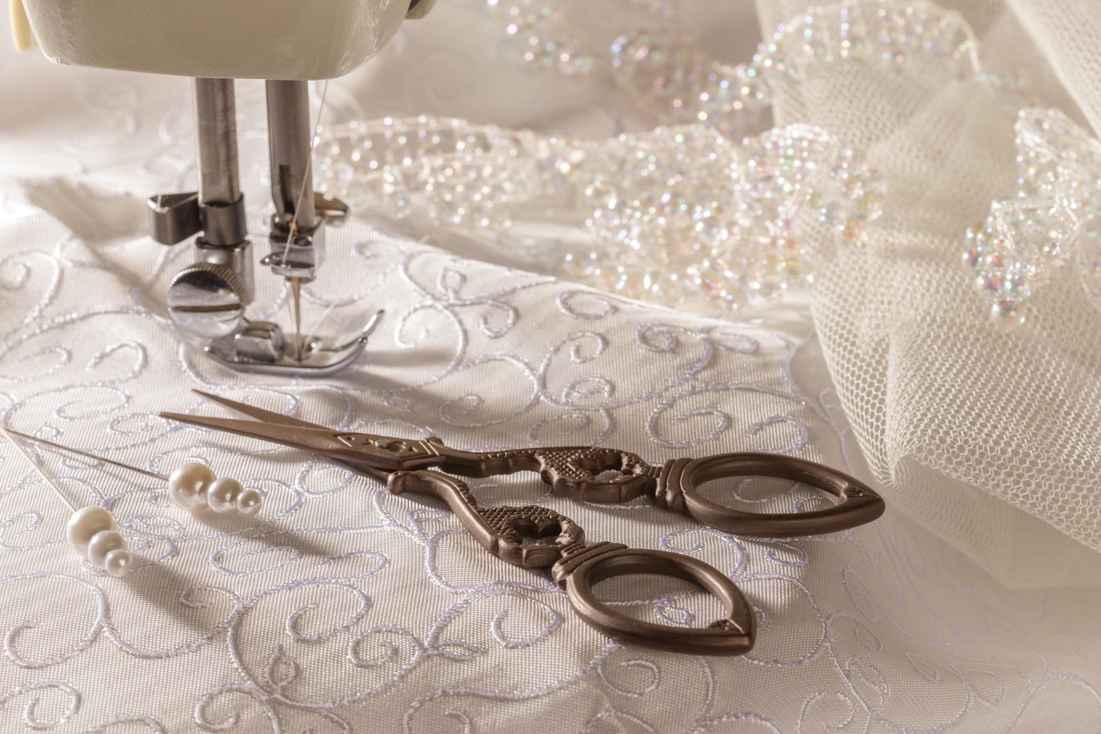 Antique dressmaking scissors beside embellished bridal lace and beadwork.