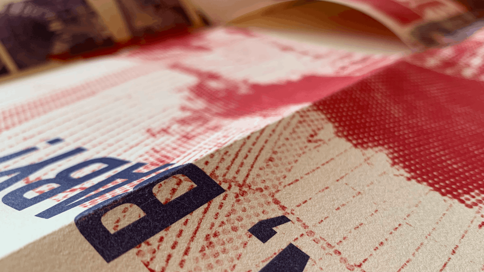 Close-up view of a textured surface with red and black printed patterns and letters on a beige background.
