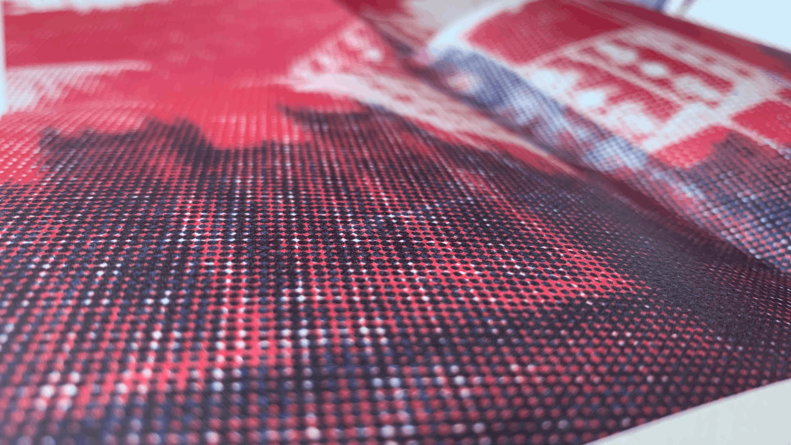 Close-up of a printed fabric or paper with a halftone dot pattern in red, black, and white, showing a blurred image with text partially visible.