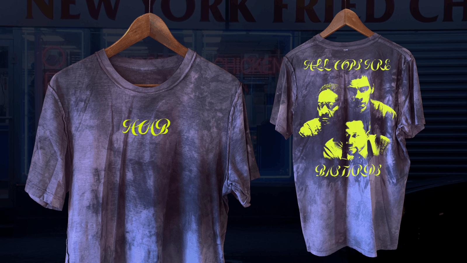 Two purple tie-dye t-shirts on wooden hangers against a dark background. The front of the left shirt has yellow cursive letters 'HCB' on the chest. The back of the right shirt features yellow cursive words 'ALL COPS ARE BASTARDS' above and below a yellow-toned graphic of three men's faces.