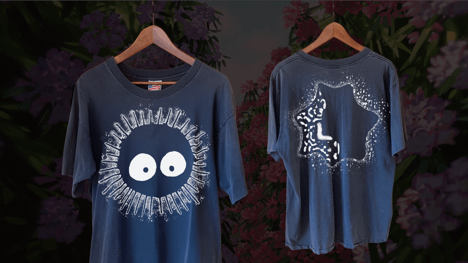 Two dark blue t-shirts hanging on wooden hangers against a floral background; the front of the left shirt shows a white circular design with large eyes and radiating lines, while the back of the right shirt features a white star-shaped pattern with an abstract design inside.
