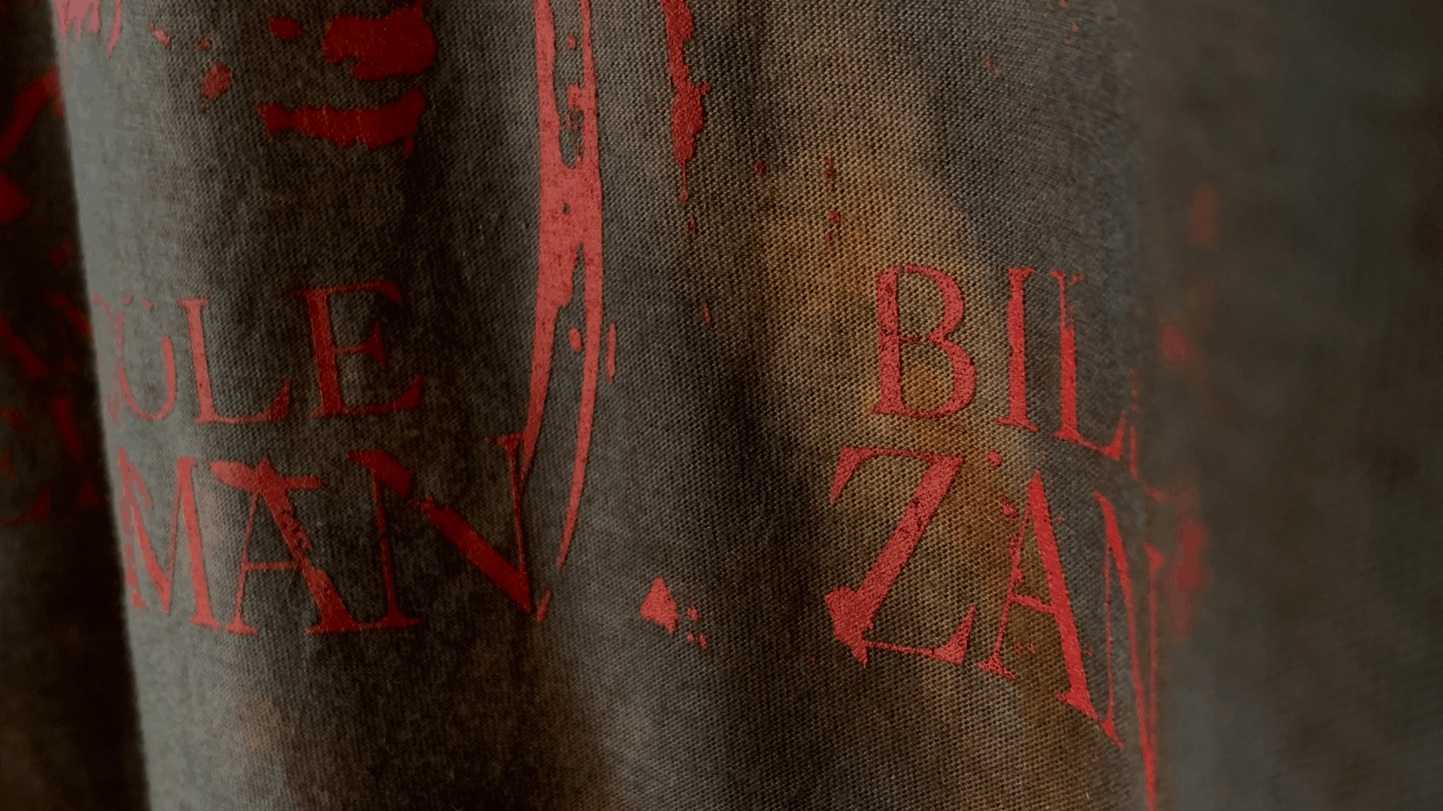 Close-up of dark fabric with faded red text reading partially 'BILLZAN' and 'MAN' printed on it.