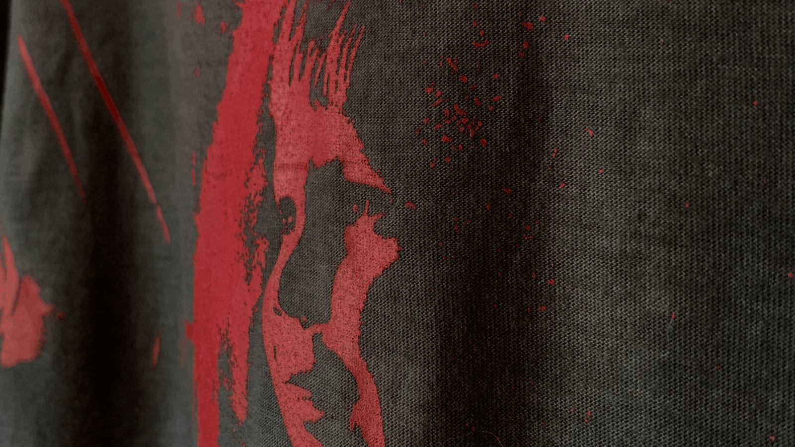 Close-up of black fabric with a faded, stylized red print resembling a person's face in profile.