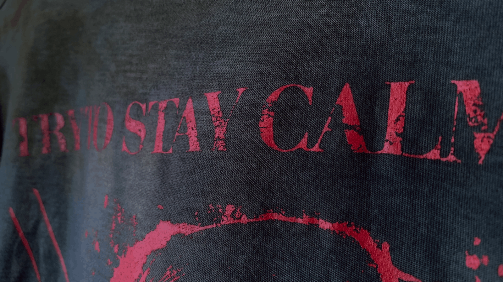 Close-up view of distressed red text reading 'TRY TO STAY CALM' printed on dark fabric.