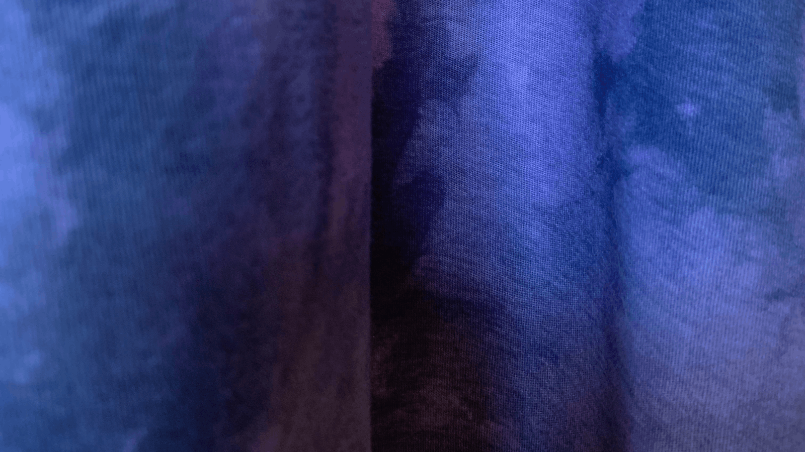Close-up of fabric with a blue and purple tie-dye pattern, showing texture and color variations.