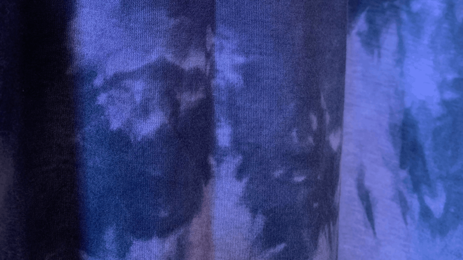 Close-up of a fabric with a blue and dark tie-dye pattern featuring soft, irregular shapes and shades blending together.