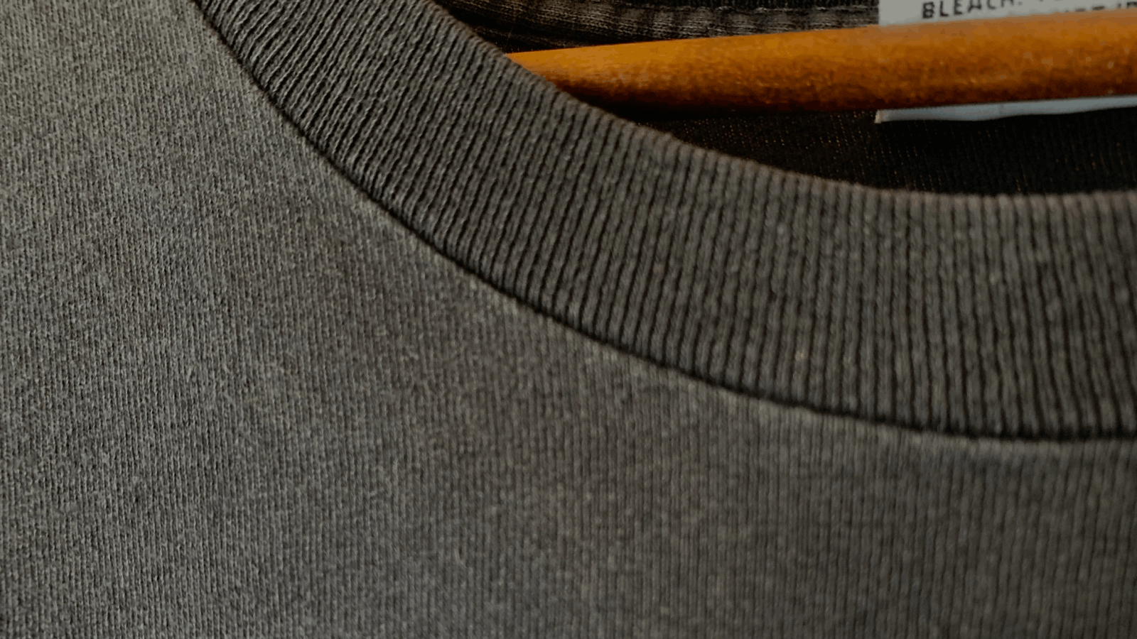 Close-up of a gray ribbed crewneck sweater on a wooden hanger.