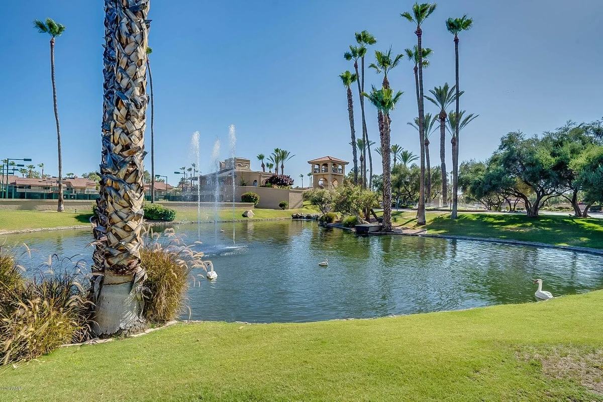 Landscaped grounds at Racquet Club with a pond, fountain and palm trees in front of community buildings.