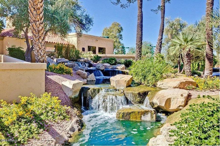 Landscaped grounds with a waterfall, desert plantings and a community building beyond.