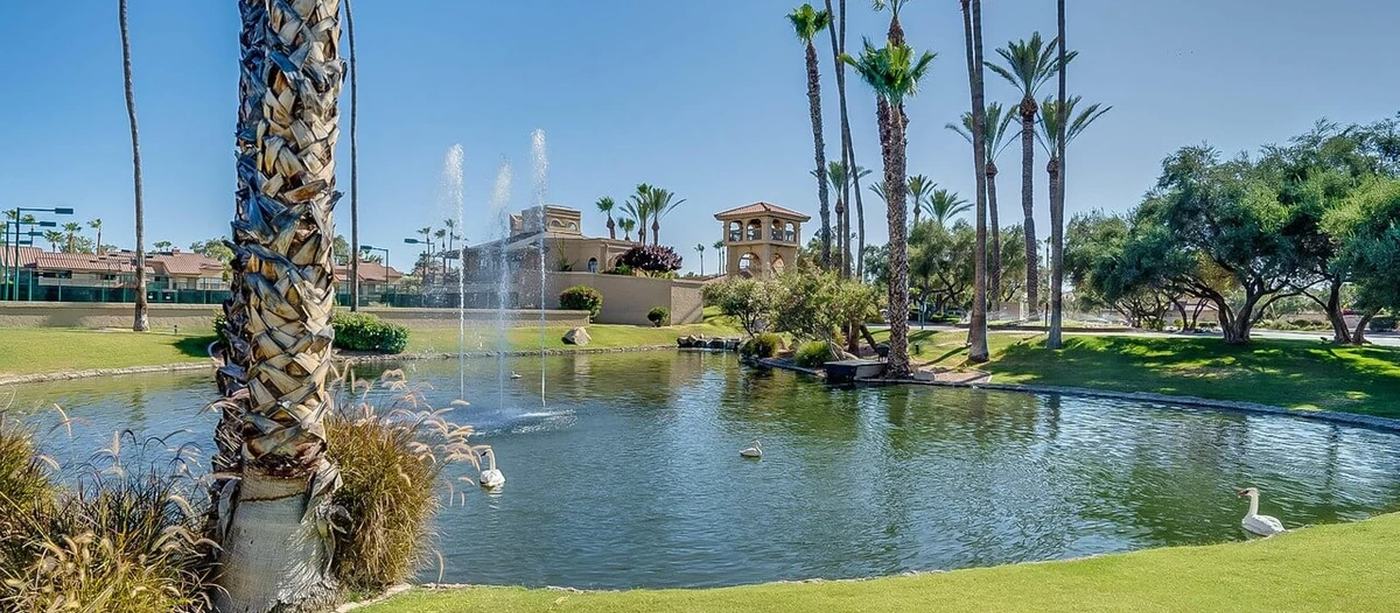 Landscaped community grounds with a pond, fountain and palm trees in front of Racquet Club buildings.