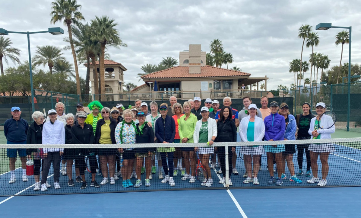 St. Paddy's Day Tennis Mixer participants gathered behind the net on a cloudy day.