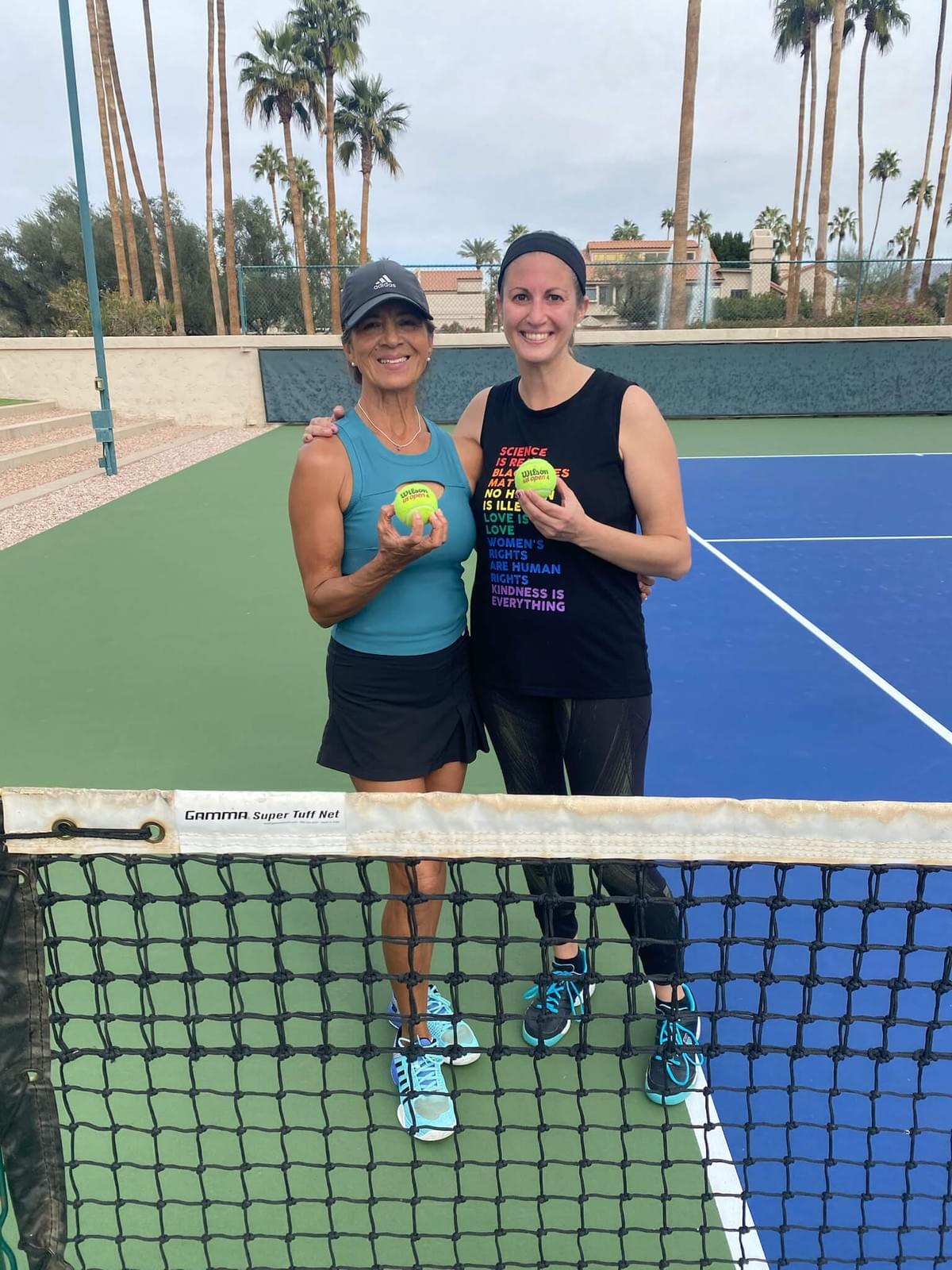 Two players holding tennis-themed awards behind the net at the 2025 women's singles championship.