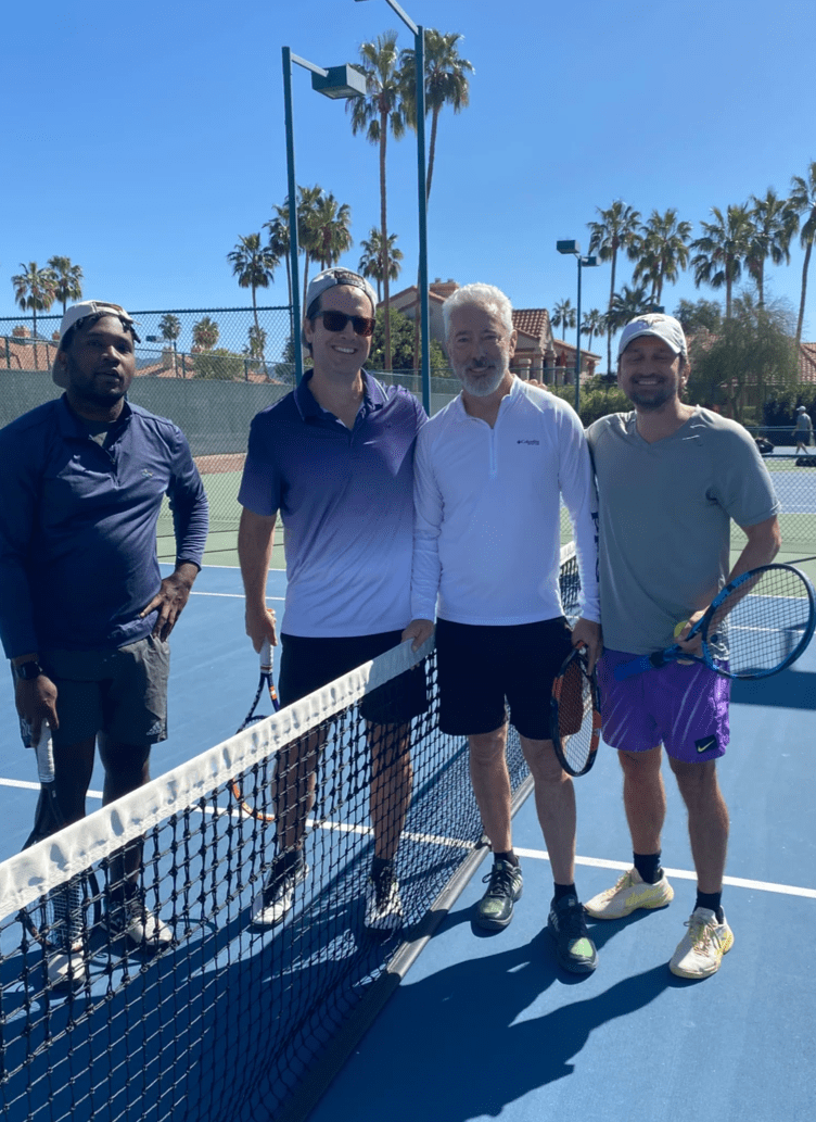 Four tournament participants posing beside the net on a blue court.