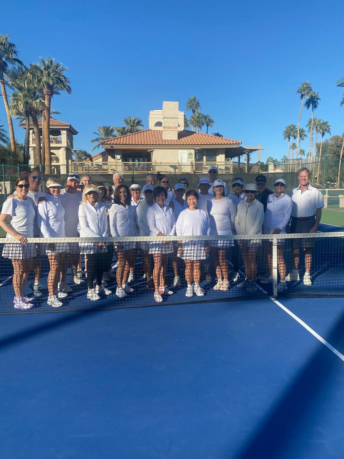Tennis event participants lined up across a court with the clubhouse behind them.