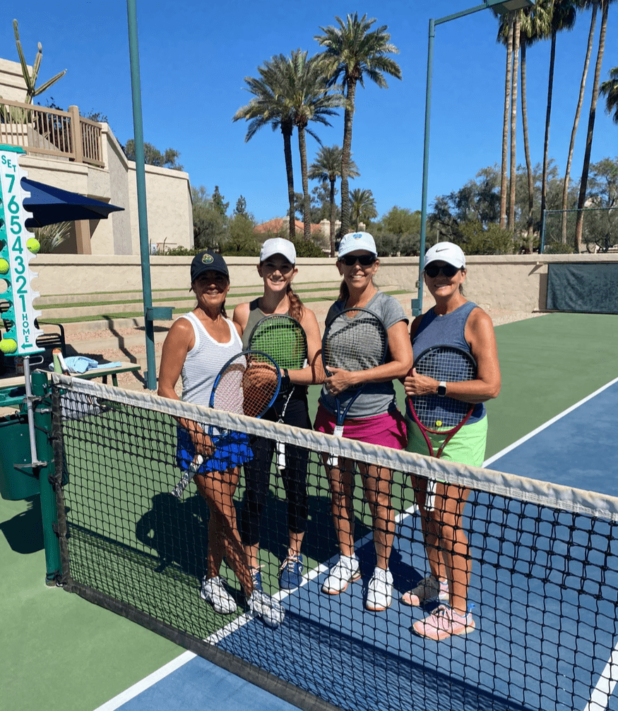 Four tournament participants with racquets standing behind the net near the clubhouse.
