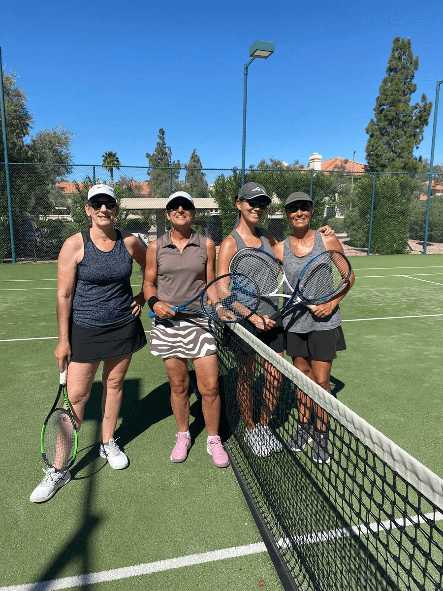 Four tournament participants with racquets gathered beside the net on a green court.