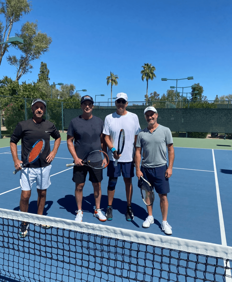 Four tournament participants standing behind the net on a blue tennis court.