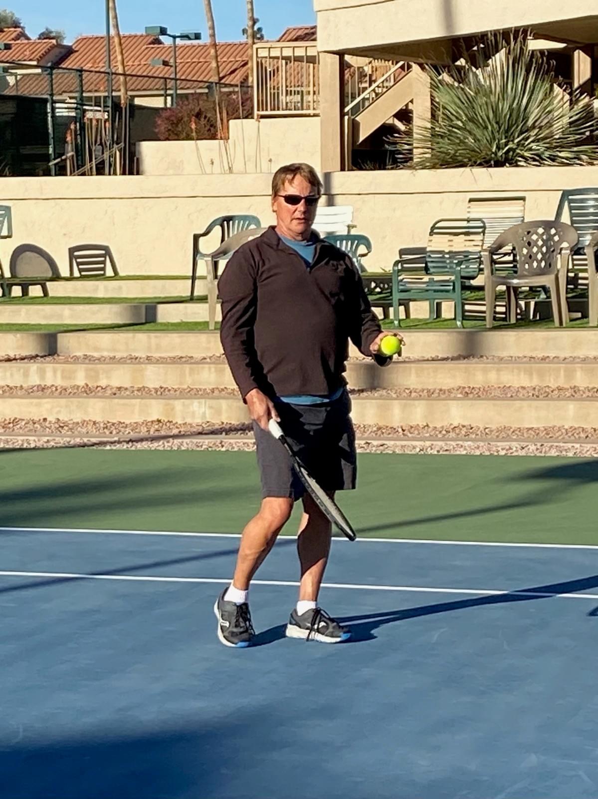 A player in dark clothing holding a racquet and tennis ball on court.