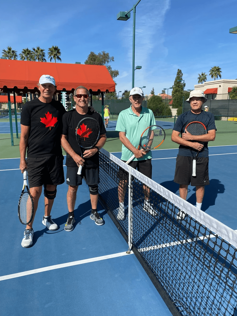 Four players with racquets standing at the net after the 2022 over-60 final.