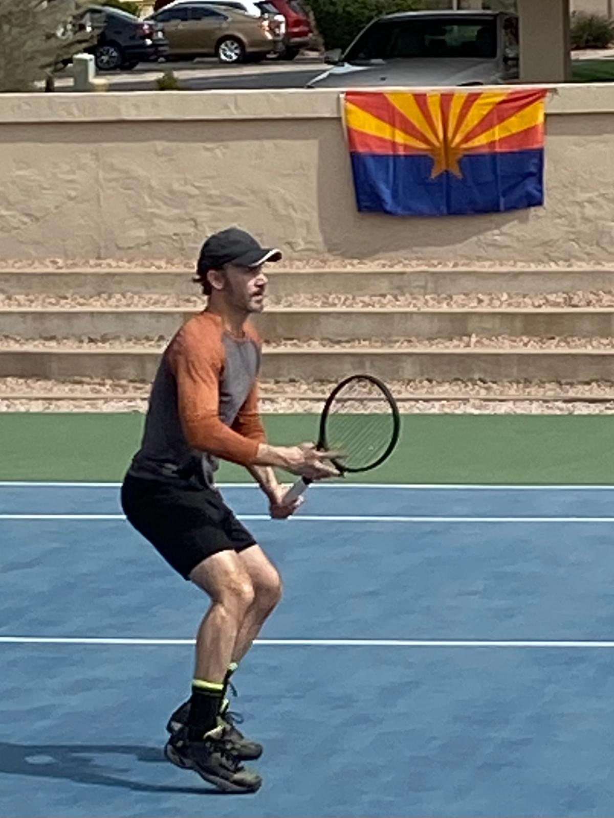 A player preparing to return a ball with an Arizona flag visible behind the court.