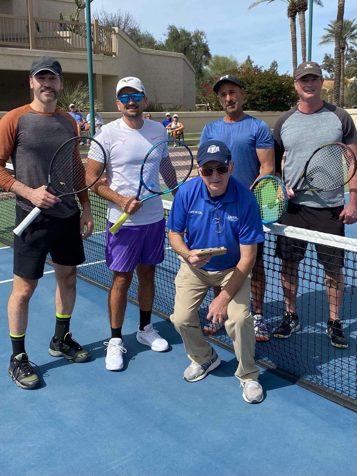 Players and an event participant posing beside the net after the 2022 men's open final.
